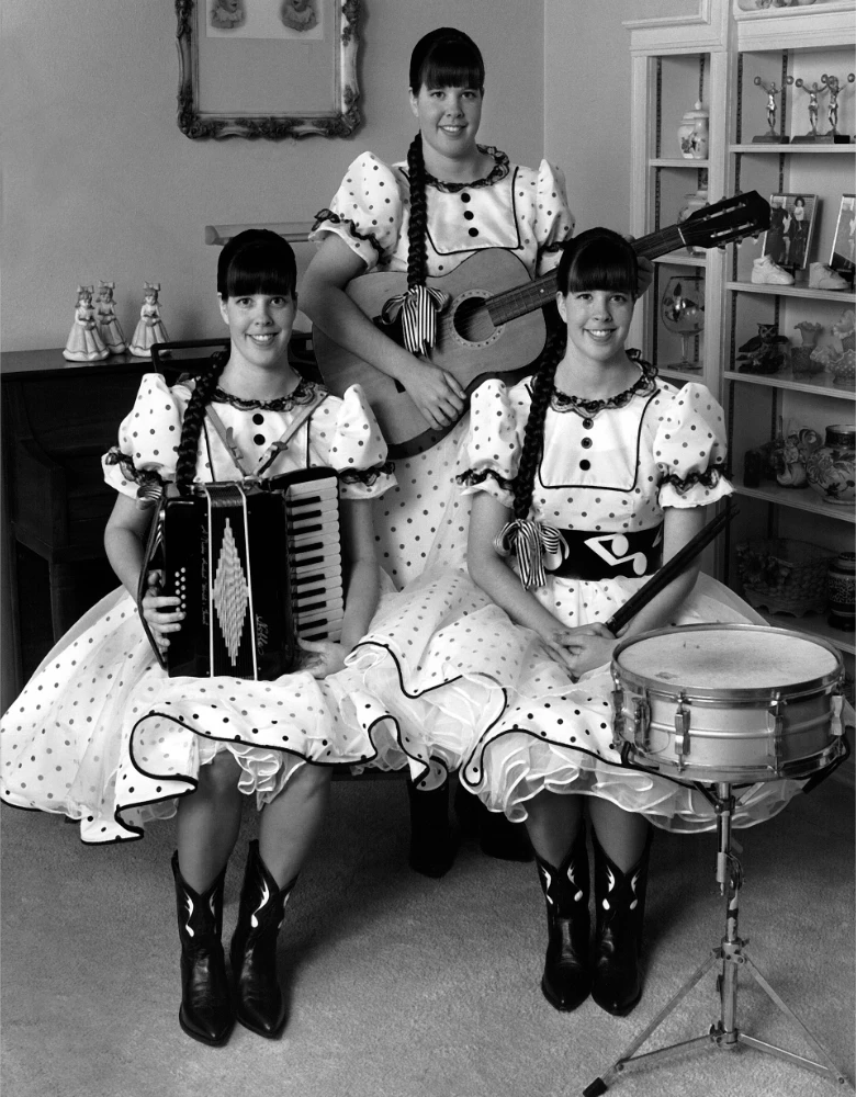 Triplets in square dance dresses pose with their band instruments.